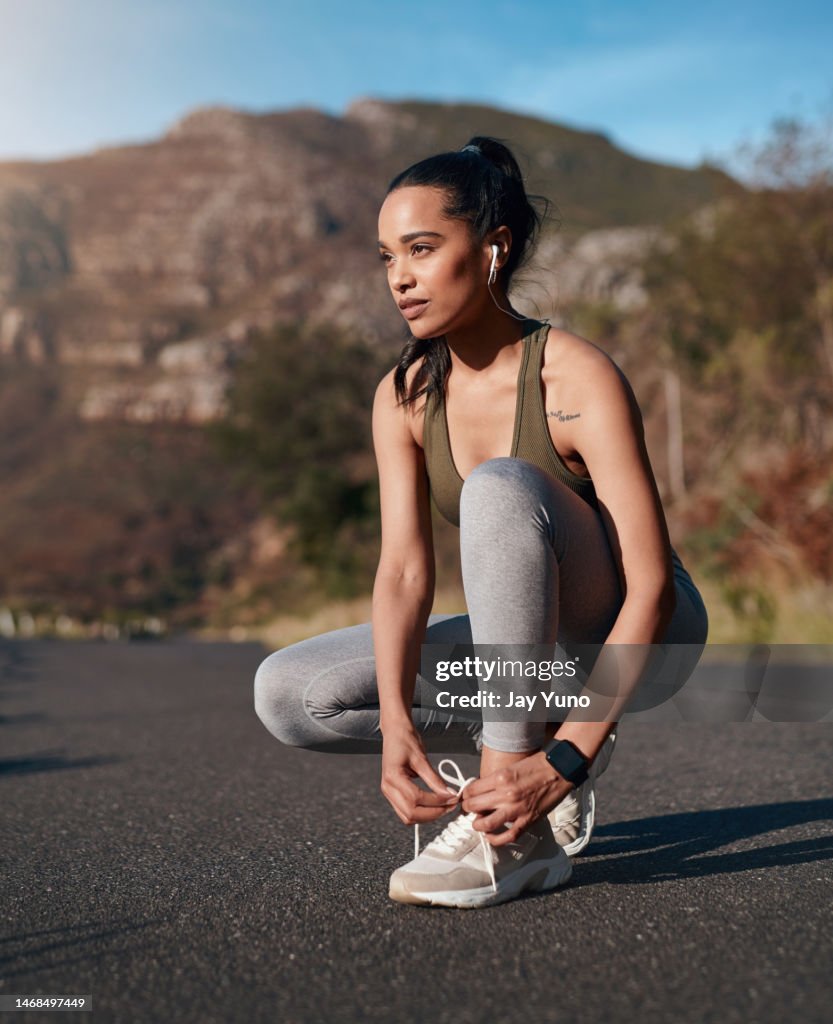 Shoes, road and runner woman getting ready for training, exercise or mountain running in sports sneakers and fashion. Young athlete or person tying her laces with cardio, fitness or workout music