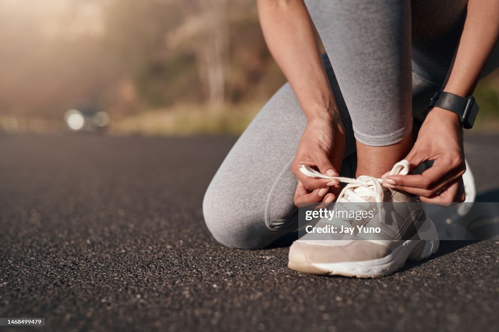 Fitness, road and woman tie her sneakers before training for a running marathon, race or competition. Sports, workout and female athlete ready to start an outdoor cardio exercise for health in street