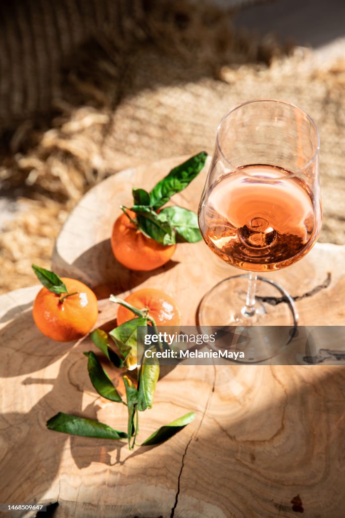 Roséweinglas auf mediterranem Stuhl mit Clementinen-Zitrusfrüchten im Sonnenschein