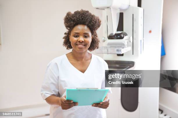 jeune infirmière debout dans la salle d’examen - blouse dexamen médical photos et images de collection