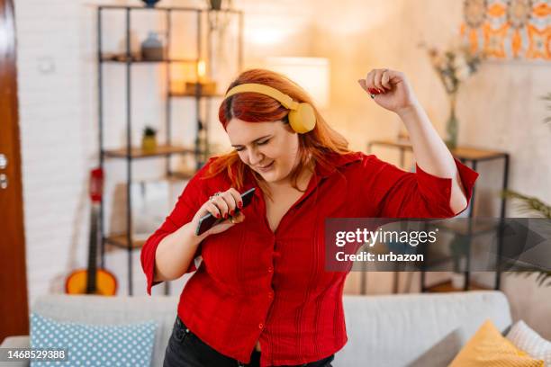 young woman singing and dancing in the living room - fat woman dancing stockfoto's en -beelden