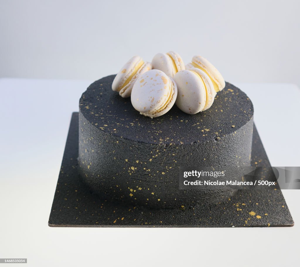 Black birthday cake decorated with gold macarons white background