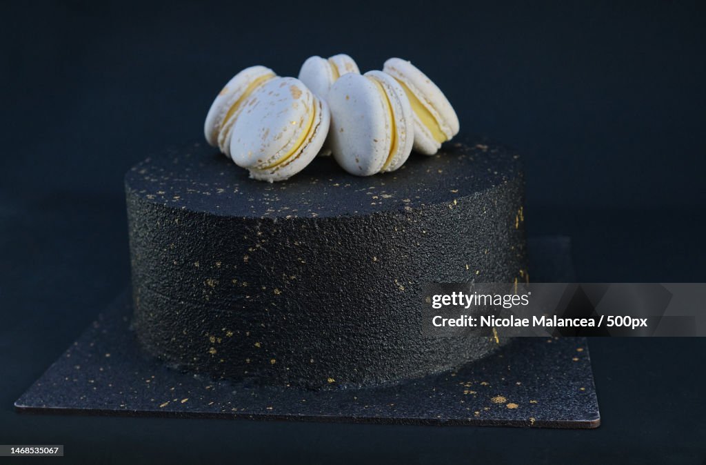 Black birthday cake decorated with gold macarons dark background