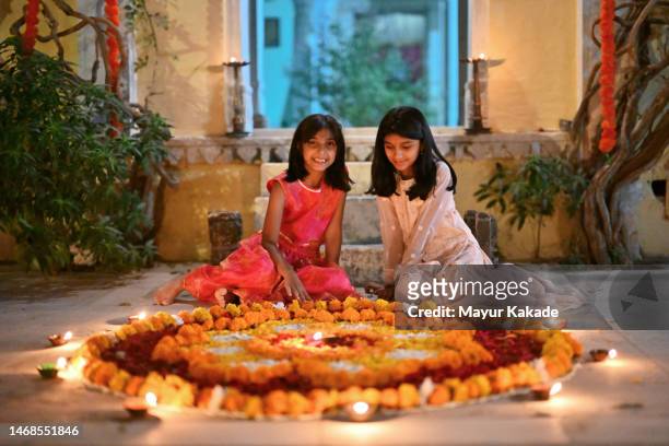 two cute indian girls dressed in traditional wear, lighting oil lamps on a rangoli at the entrance of a temple during a festival - dussehra bildbanksfoton och bilder