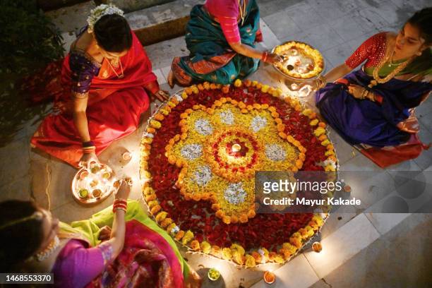 high angle view of beautiful indian women in saris (indian traditional wear) decorating rangoli with oil lamps (diya) - diya oil lamp stock pictures, royalty-free photos & images
