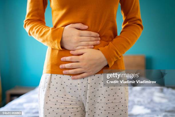 an unrecognizable woman is holding her stomach due to a strong pain - bladder stock pictures, royalty-free photos & images