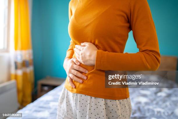 an unrecognizable woman is holding her stomach due to a strong pain - digestion stockfoto's en -beelden