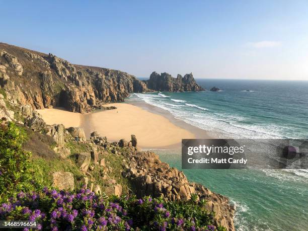 Person walks on sand revealed at high tide at Pedn Vounder beach near Treen and the Logan Rock on February 13, 2023 in Cornwall, England. The county...