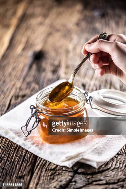 honey dripping from spoon in glass jar. healthy organic thick honey dipping from the spoon, closeup. - sugar in glass stock pictures, royalty-free photos & images