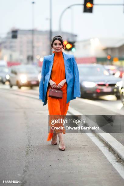 Alexandra Pereira wears a neon orange halter high neck / backless / long silk dress, a blue blazer jacket, diamonds rings, a brown shiny leathers...