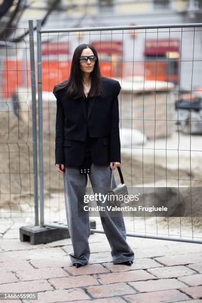 Guest is seen wearing black sunglasses, a black cropped, padded shoulder straps blazer, a black long-sleveed body with white bottoms and grey wide...