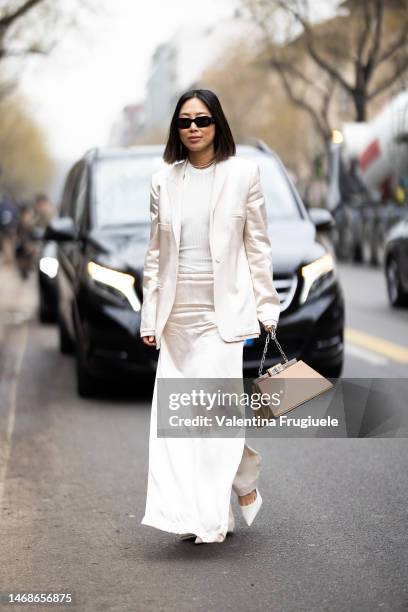 Aimee Song is seen wearing black Prada sunglasses, a pearl necklace and a lettering necklace, a white cream satin blazer, a white shirt, a white...