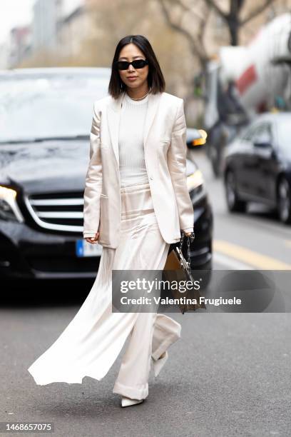 Aimee Song is seen wearing black Prada sunglasses, a pearl necklace and a lettering necklace, a white cream satin blazer, a white shirt, a white...