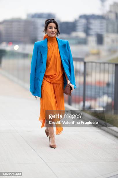 Guest is seen wearing a draped turtleneck orange dress, a light blue jacket over the shoulders, brown pumps and mini handbaoutside the Alberta...