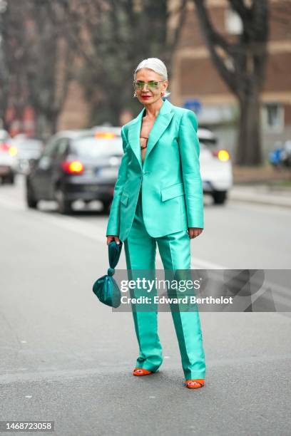 Grece Ghanem wears green sunglasses, gold and pink earrings, a mint green silk blazer jacket, matching mint green suit suit pants, a dark green silk...
