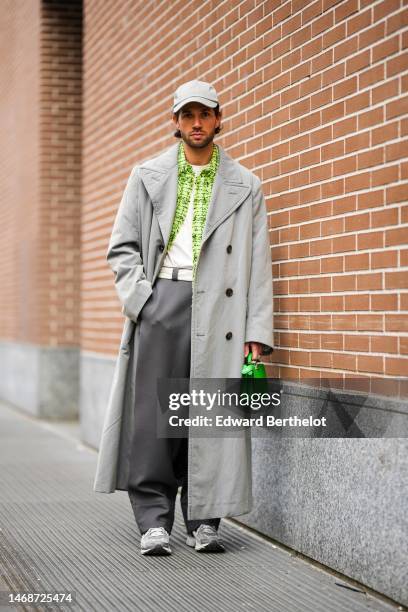 Roques wears a pale gray cap, a white t-shirt, a pale green and dark green print pattern shirt, a pale gray long coat, a white shiny leather belt, a...