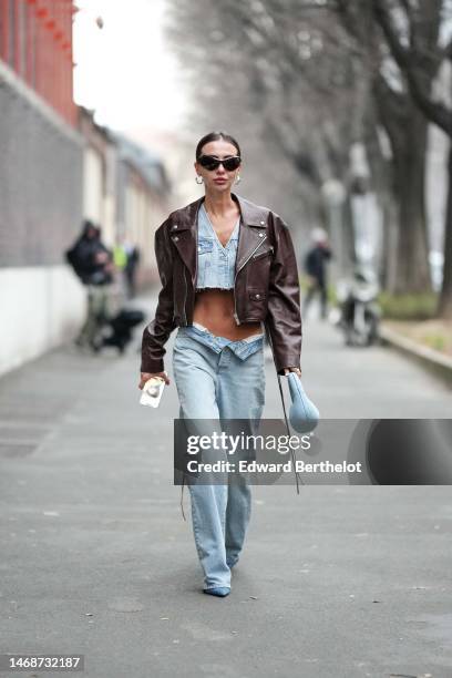 Guest wears black butterfly sunglasses, silver earrings, a pale blue denim cargo cropped ripped top, pale bue denim large pants, a pale blue denim...