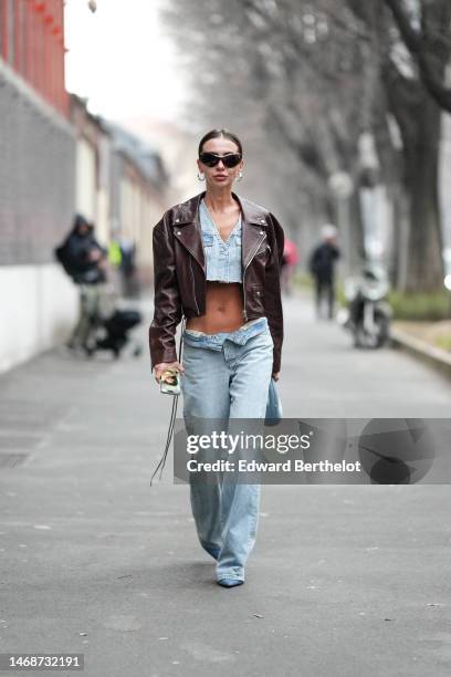 Guest wears black butterfly sunglasses, silver earrings, a pale blue denim cargo cropped ripped top, pale bue denim large pants, a pale blue denim...