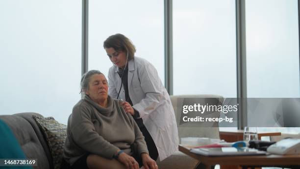 female doctor visiting female senior patient at home and listening her heartbeat and lungs with stethoscope - listening to heartbeat 個照片及圖片檔