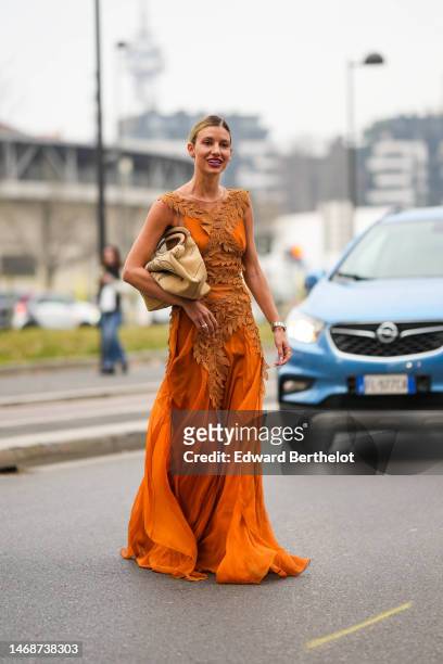 Guest wears rhinestones logo earrings from Dior, an orange with brown embroidered pattern brown yoke sleeveless / long dress, a beige matte leather...