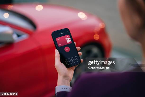 over the shoulder view of young asian woman using mobile app device on smartphone to unlock the doors of her intelligence car in car park. wireless and modern technology. smart car with digital car key concept - smart car - fotografias e filmes do acervo