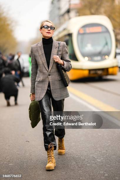 Guest wears black sunglasses, a black wool turtleneck pullover, a brown checkered print pattern blazer jacket, a khaki quilted pattern puffer jacket,...
