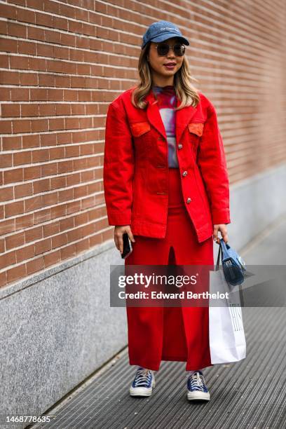 Guest wears a blue denim cap, black sunglasses, a red / purple / blue print pattern tulle high neck t-shirt, a red denim jacket, a matching red slit...