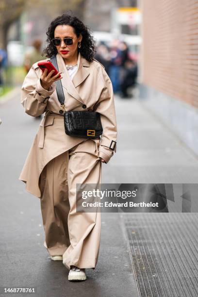 Guest wears black sunglasses, silver earrings, a white t-shirt, a white pearls necklace, a beige long asymmetric coat , beige large suit pants, white...