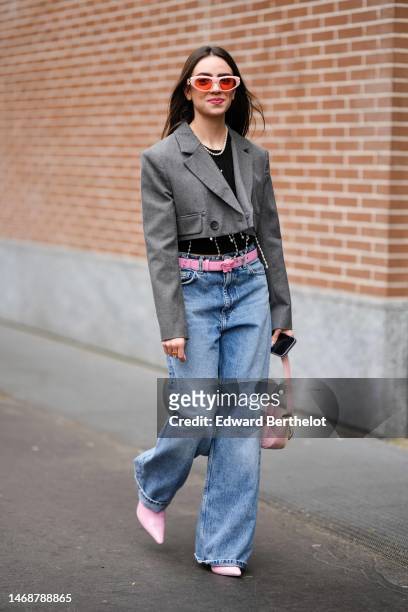 Guest wears pale pink and red sunglasses, a black cropped t-shirt, a dark gray cropped blazer jacket with rhinestones embroidered fringed borders, a...