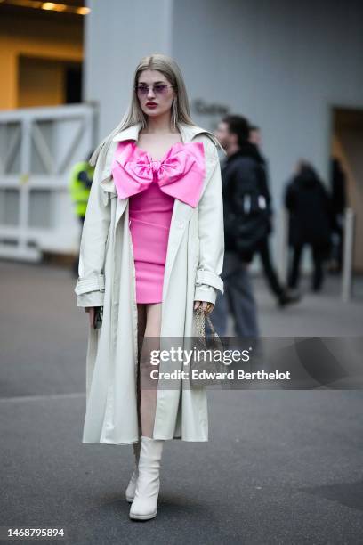 Guest wears pink sunglasses, rhinestones fringed pendant earrings, a neon pink silk short dress with an oversized knot chest, a beige long coat, a...