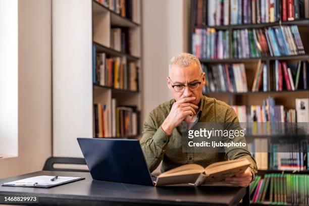 man sitting inside a library alone doing research. - hand on chin thinking stock pictures, royalty-free photos & images