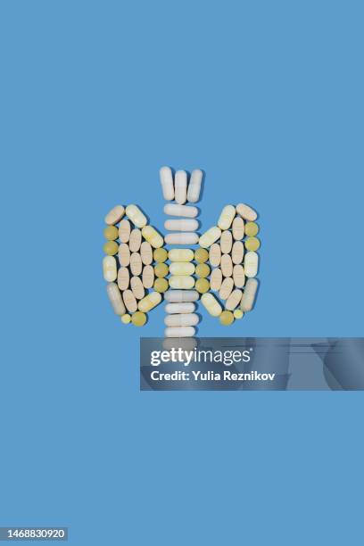 pills in shape of human thyroid gland on the blue background - thyroid cancer stock pictures, royalty-free photos & images