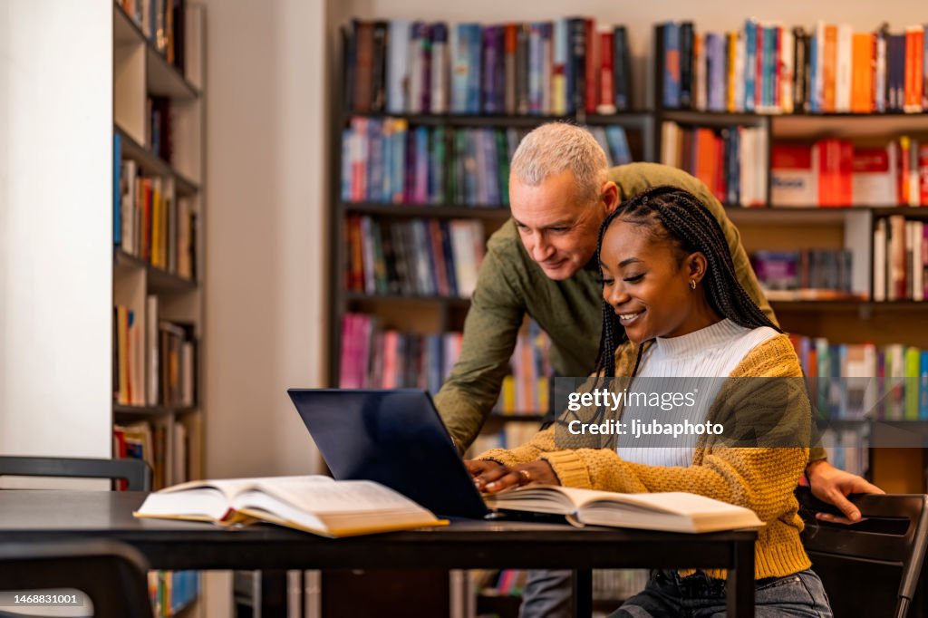 High School Tutor Giving Male Student One To One Tuition At Desk