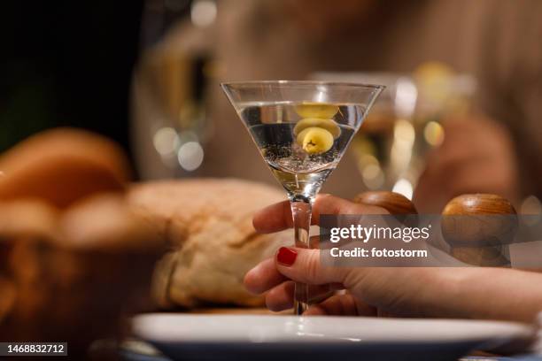 woman enjoying a martini with green olives during a dinner party with friends - martini stockfoto's en -beelden