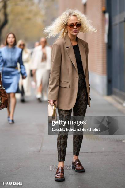 Guest wears brown sunglasses, a black t-shirt, a brown blazer jacket, black and brown FF monogram print pattern legging pants from Fendi, a beige...