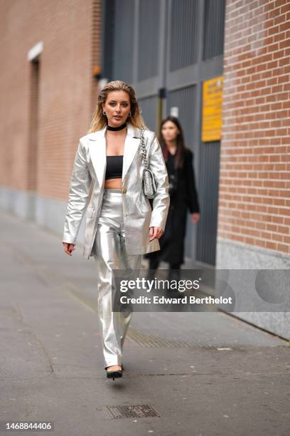 Guest wears silver earrings, a black necklace, a black shoulder-off / cropped top, a silver shiny leather blazer jacket, matching silver shiny...