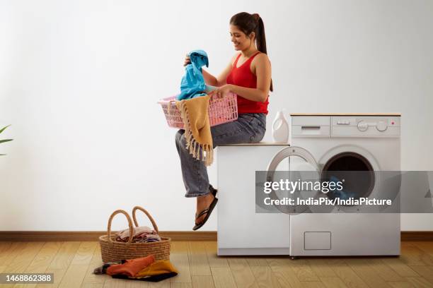 young woman sitting near washing machine with laundry basket - laundry basket stock pictures, royalty-free photos & images