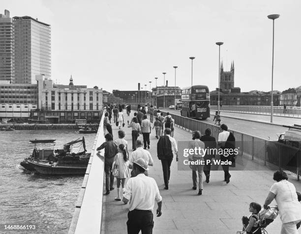 Pedestrians walk along the path beside traffic crossing London Bridge, spanning the River Thames, linking the City of London and Southwark, with the...