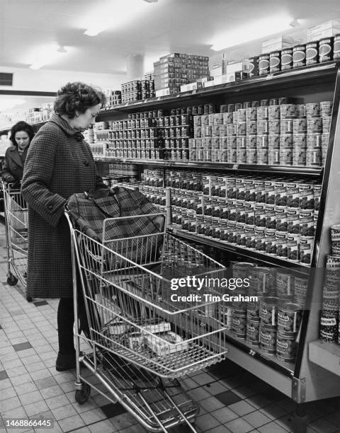 An shopper pushing supermarket trolley past shelves of tinned tomatoes in the canned vegetables aisle of J Sainsbury's supermarket, in Sutton,...