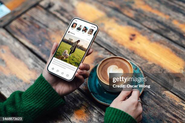 elevated view of young woman connecting with social media app on smartphone while drinking coffee - dating stockfoto's en -beelden