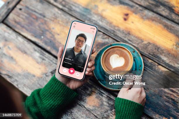 elevated view of young woman looking for love with online dating app on smartphone while drinking coffee - dating stockfoto's en -beelden