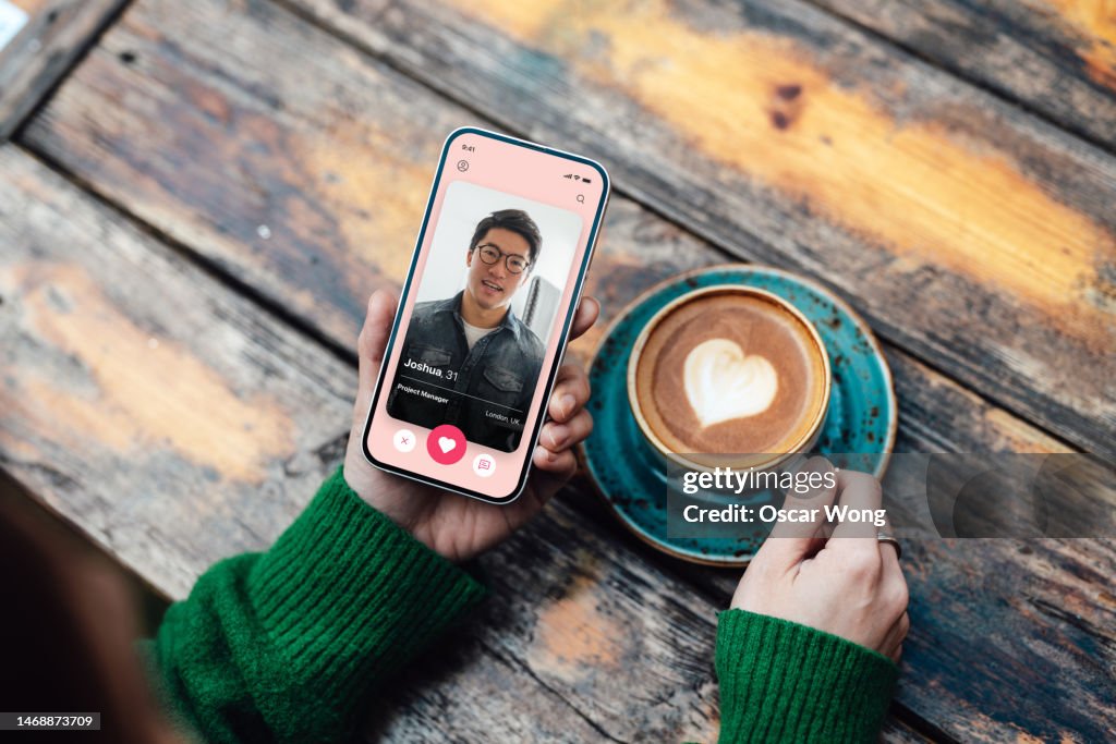 Elevated view of young woman looking for love with online dating app on smartphone while drinking coffee