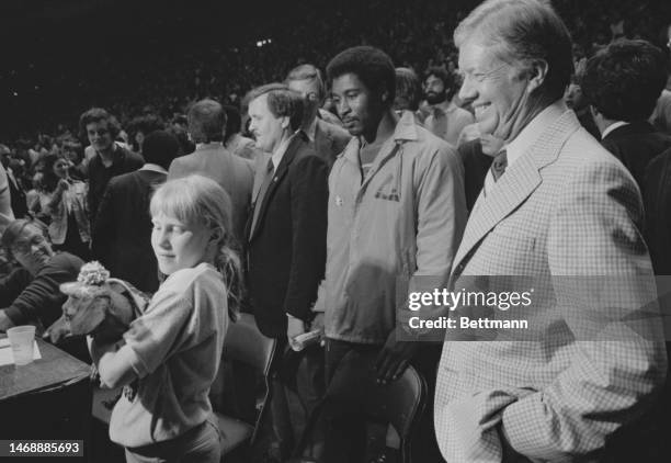 President Carter looks over his daughter Amy's shoulder as she holds the Washington Bullets mascot, Tiny, at the end of the NBA playoff game between...