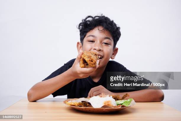 boy eating food while sitting against white background,bali,indonesia - heri mardinal stock pictures, royalty-free photos & images