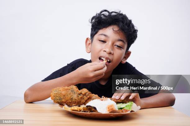 boy eating food while sitting on table against white background,bali,indonesia - heri mardinal stock pictures, royalty-free photos & images