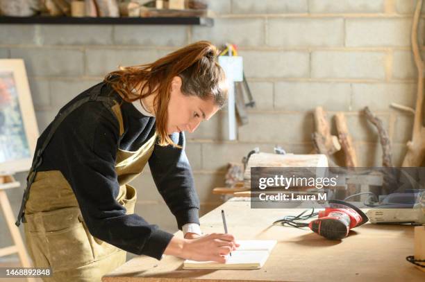 woman working while taking notes in a carpentry workshop - independence imagens e fotografias de stock