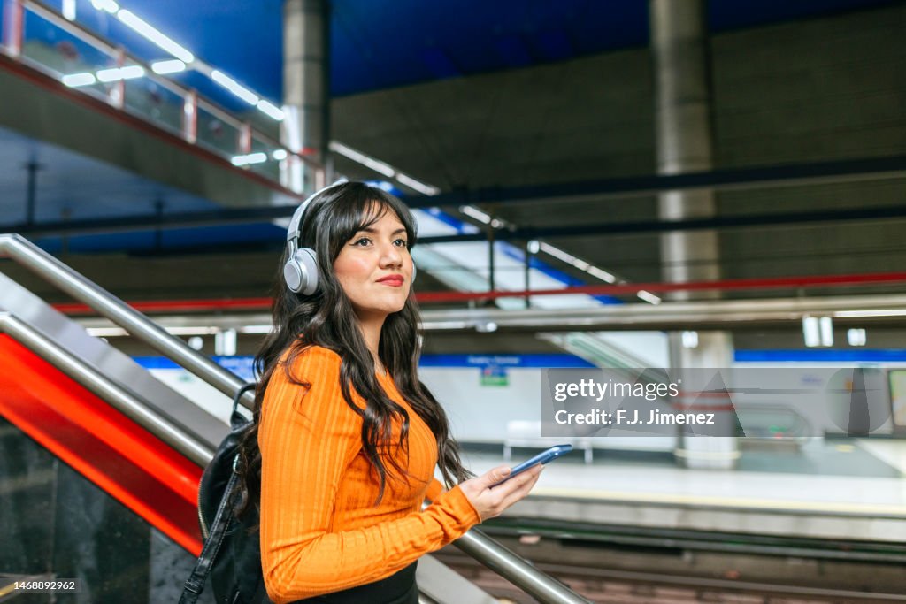 Woman walking in subway station with mobile and headphones
