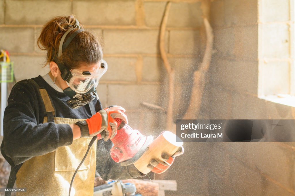 Female carpenter with protective gear polishing wood in a workshop