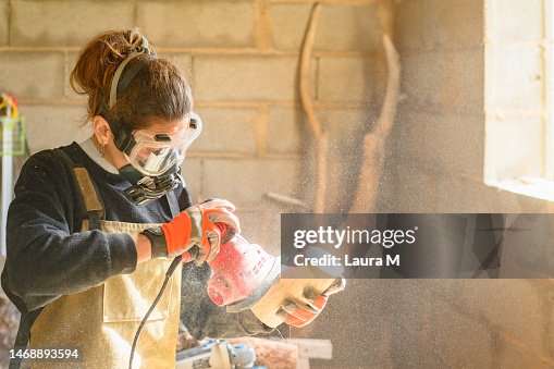 Female carpenter with protective gear polishing wood in a workshop Female carpenter with protective gear polishing wood in a workshop