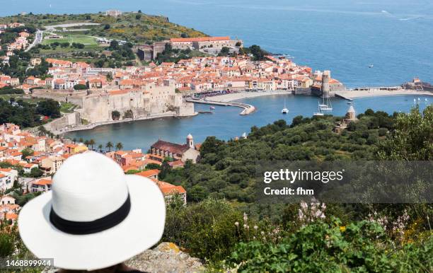 tourist with sun hat and view to a village near the mediterranean sea (collioure/ cote vermeille, france) - pirineos fotografías e imágenes de stock